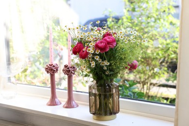 Beautiful ranunculus flowers and chamomiles in vase on windowsill indoors