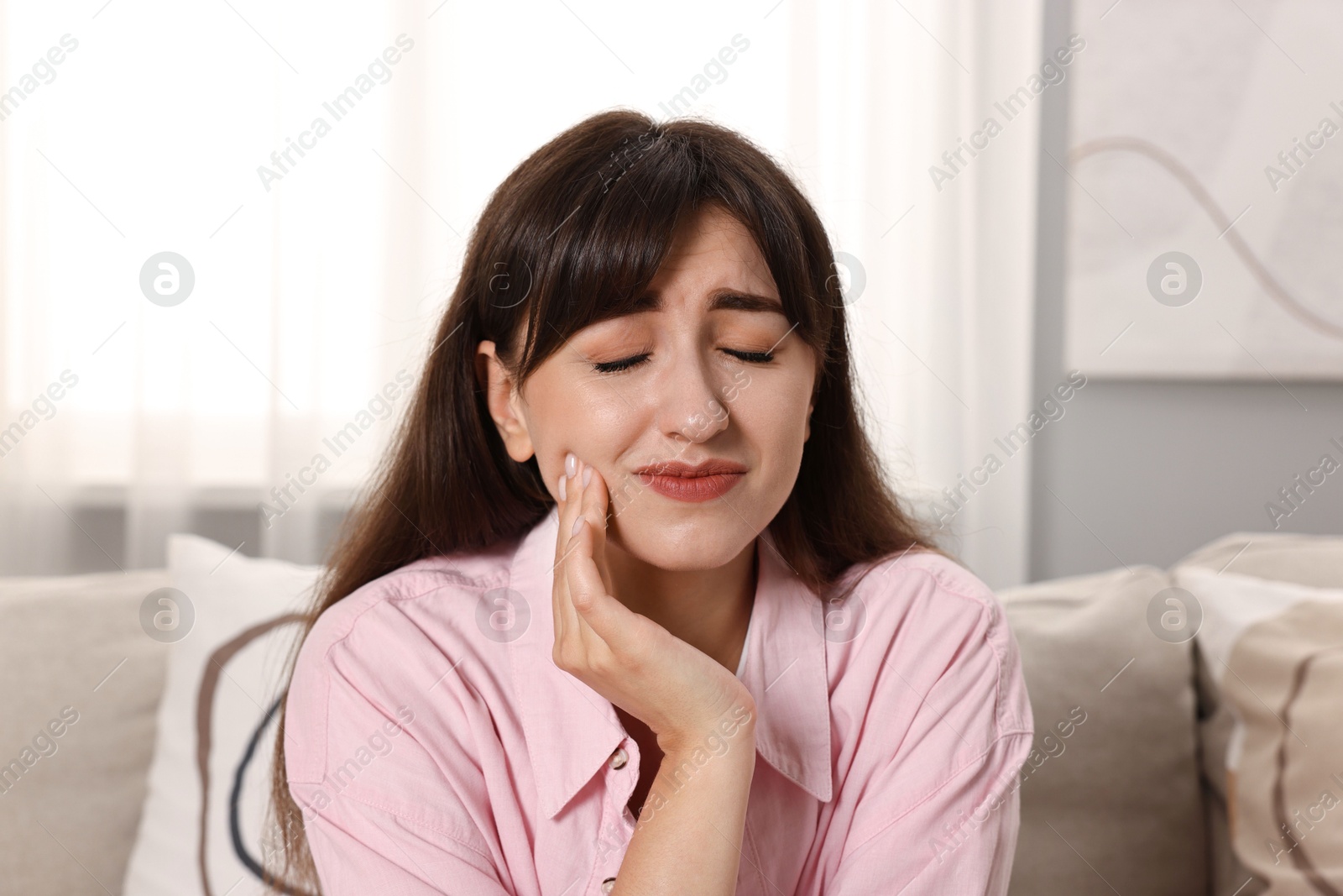 Photo of Upset young woman suffering from toothache indoors