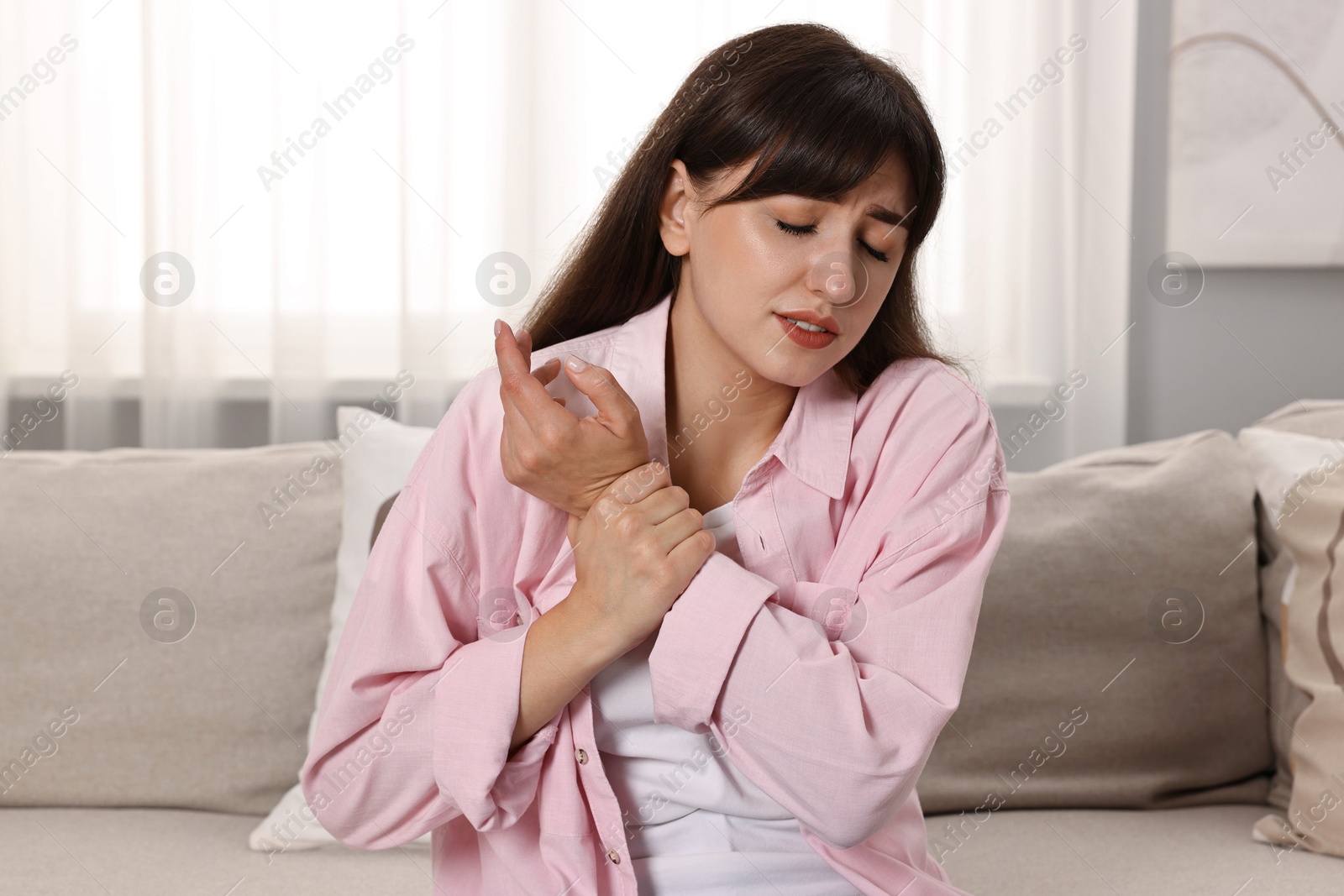 Photo of Upset woman suffering from pain in wrist on sofa at home