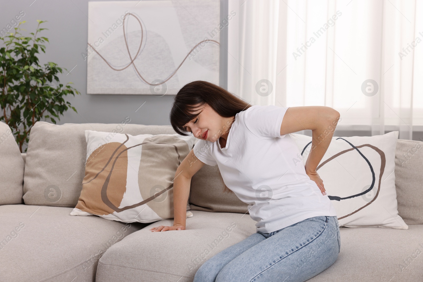 Photo of Upset woman suffering from back pain on sofa at home