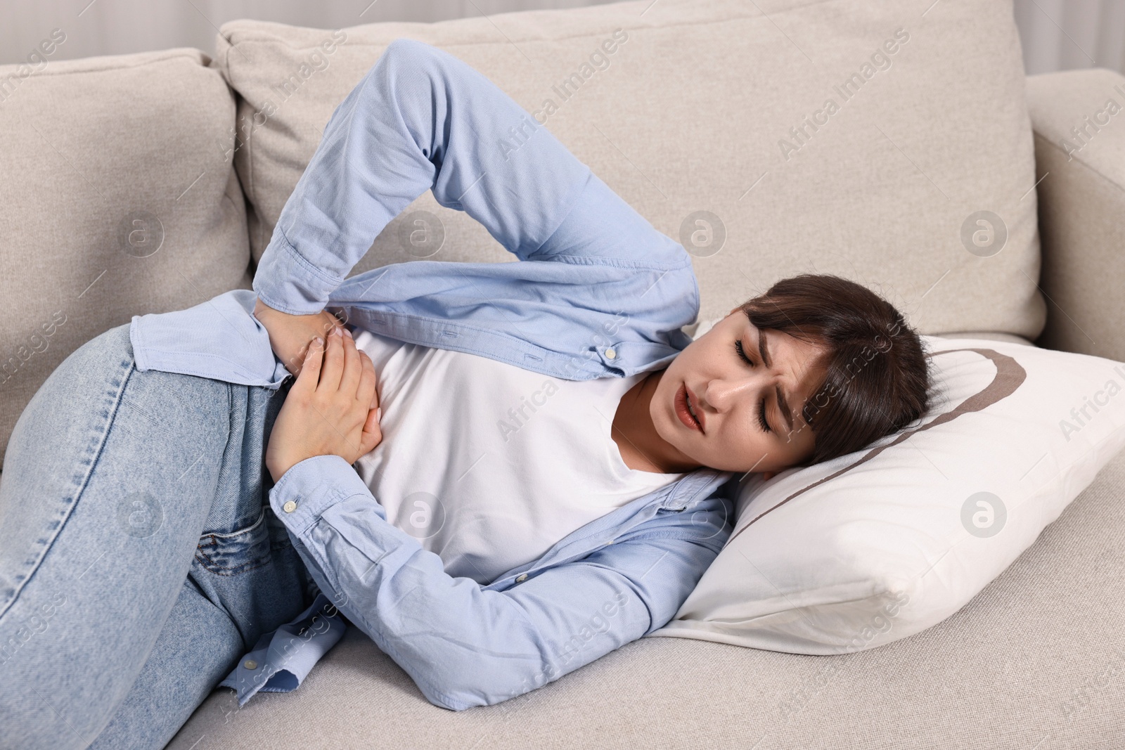 Photo of Upset woman suffering from abdominal pain on sofa at home