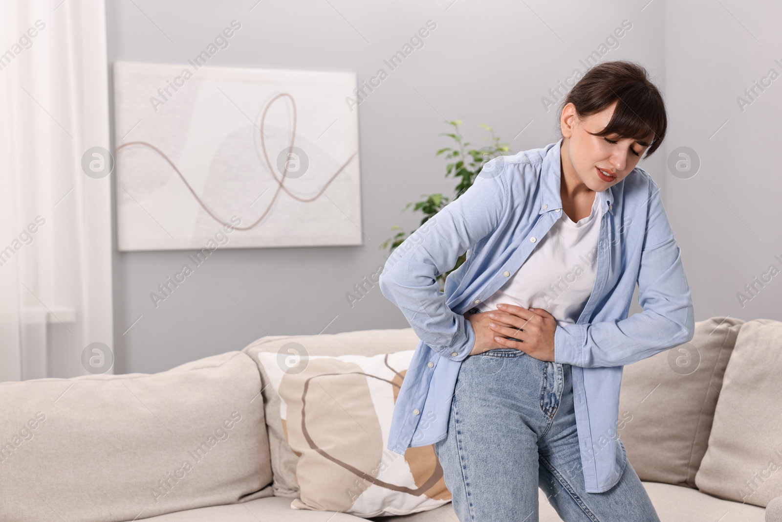 Photo of Upset woman suffering from abdominal pain at home, space for text