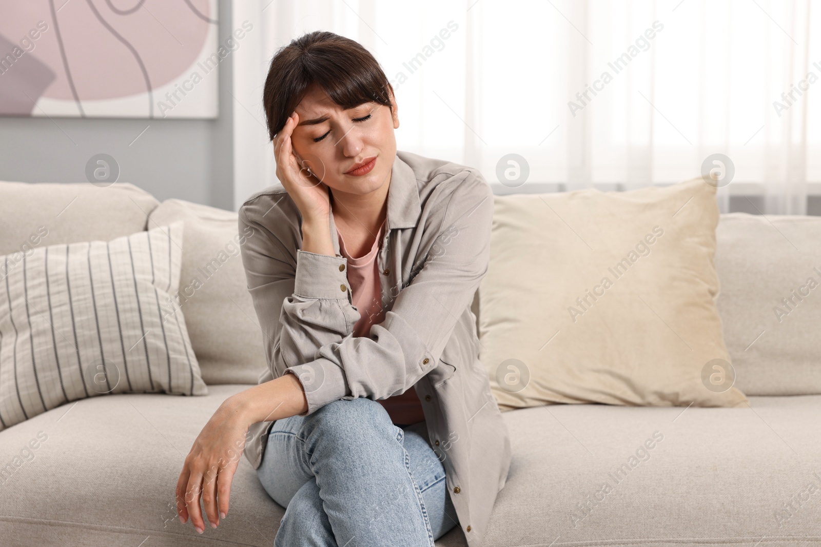 Photo of Upset woman suffering from headache on sofa at home