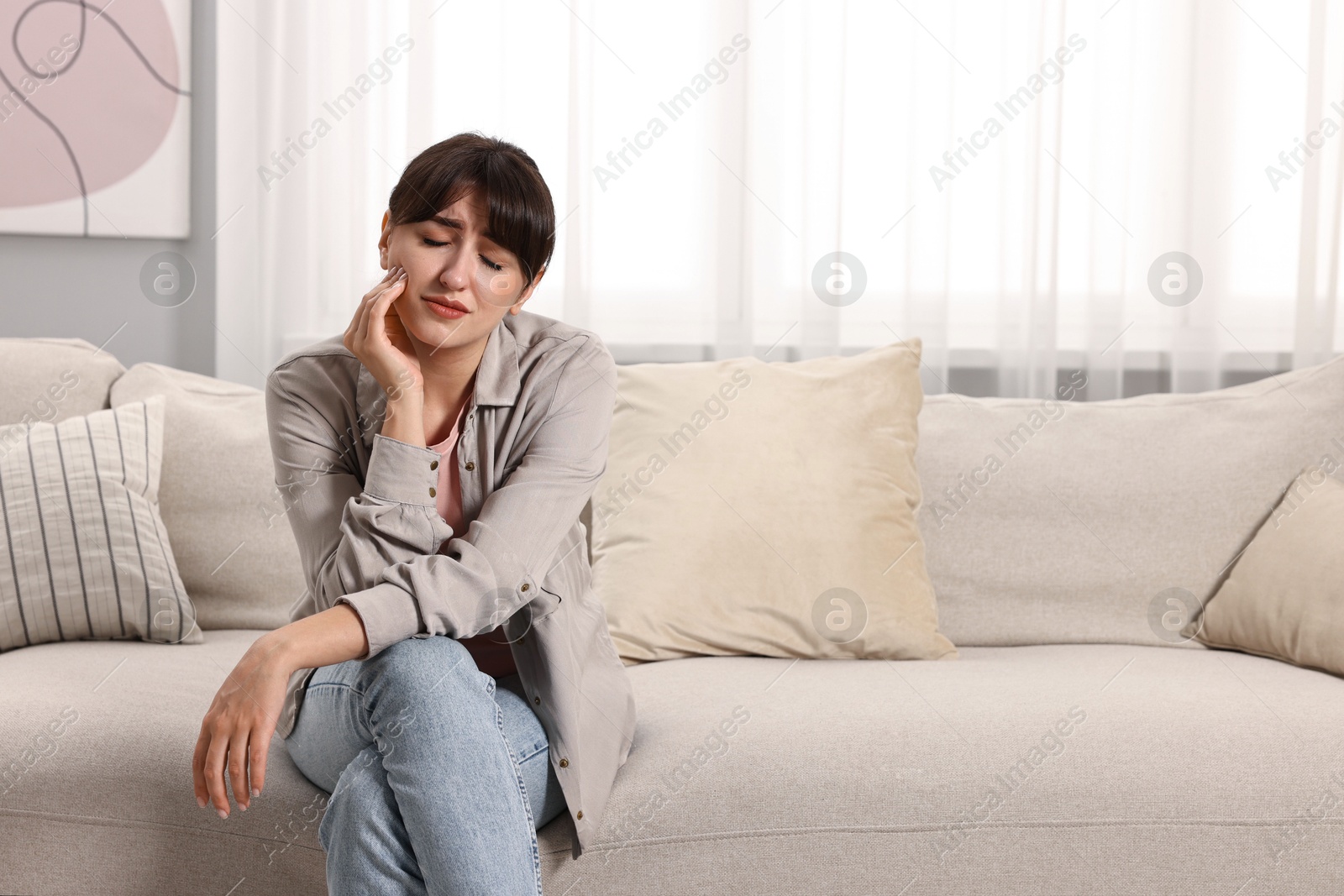 Photo of Upset woman suffering from headache on sofa at home, space for text