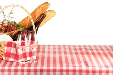 Picnic wicker basket with checkered napkin, food and bottle of wine on table against white background. Space for text