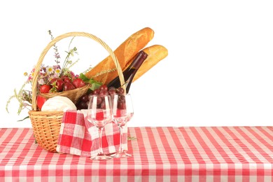 Photo of Picnic wicker basket with checkered napkin, food and bottle of wine on table against white background. Space for text