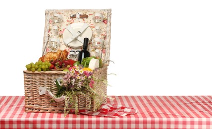 Photo of Picnic wicker basket with food, tableware, bottle of wine and flowers on table against white background. Space for text