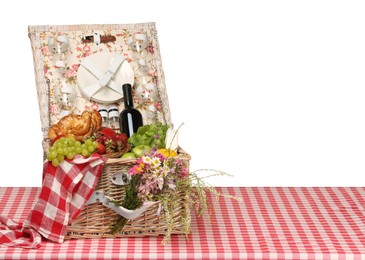 Photo of Picnic wicker basket with food, tableware, bottle of wine and flowers on table against white background. Space for text