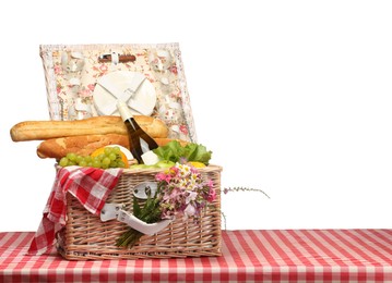 Photo of Picnic wicker basket with food, tableware, bottle of wine and flowers on table against white background. Space for text