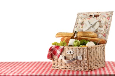 Photo of Picnic wicker basket with food, tableware, bottle of wine and napkin on table against white background. Space for text