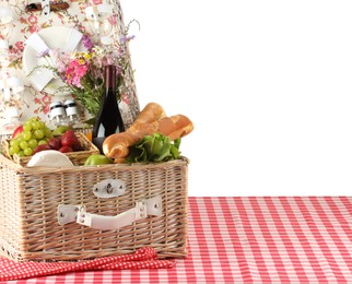 Photo of Picnic wicker basket with food, tableware, bottle of wine and flowers on table against white background. Space for text