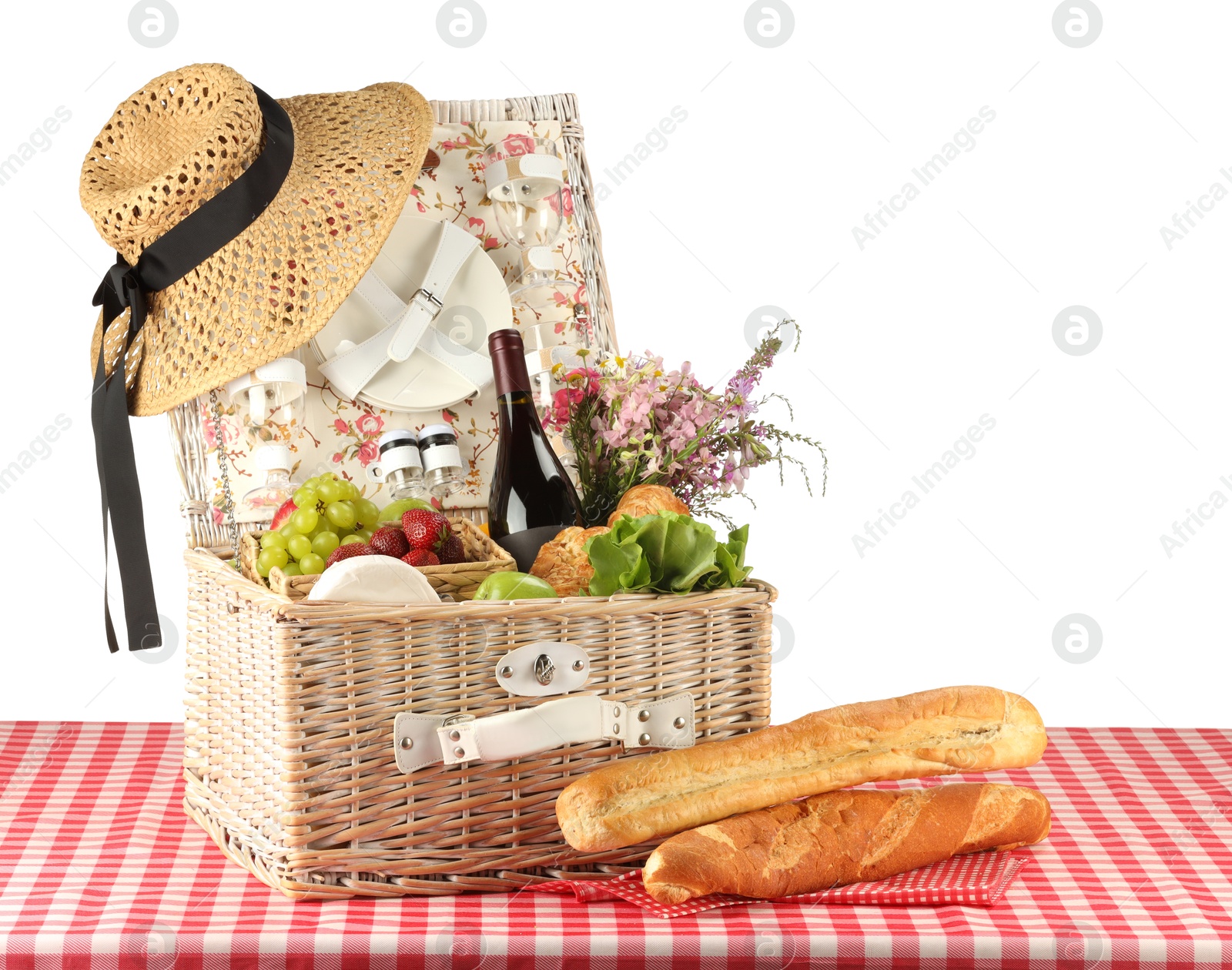 Photo of Picnic wicker basket with food, tableware, bottle of wine and flowers on table against white background