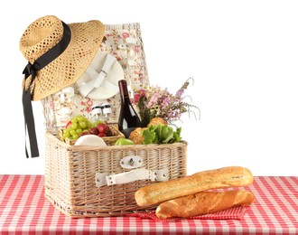 Photo of Picnic wicker basket with food, tableware, bottle of wine and flowers on table against white background