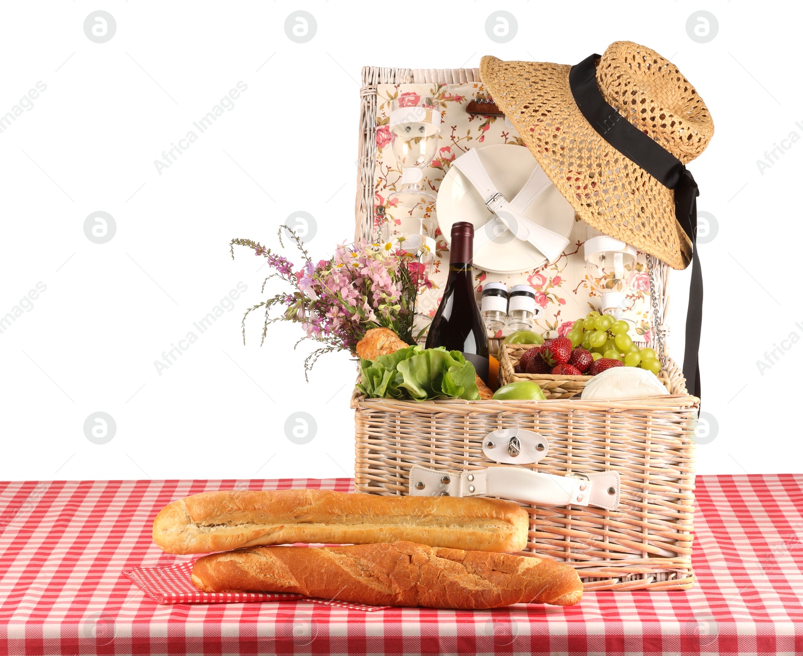 Photo of Picnic wicker basket with food, tableware, bottle of wine and flowers on table against white background