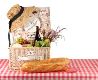 Photo of Picnic wicker basket with food, tableware, bottle of wine and flowers on table against white background