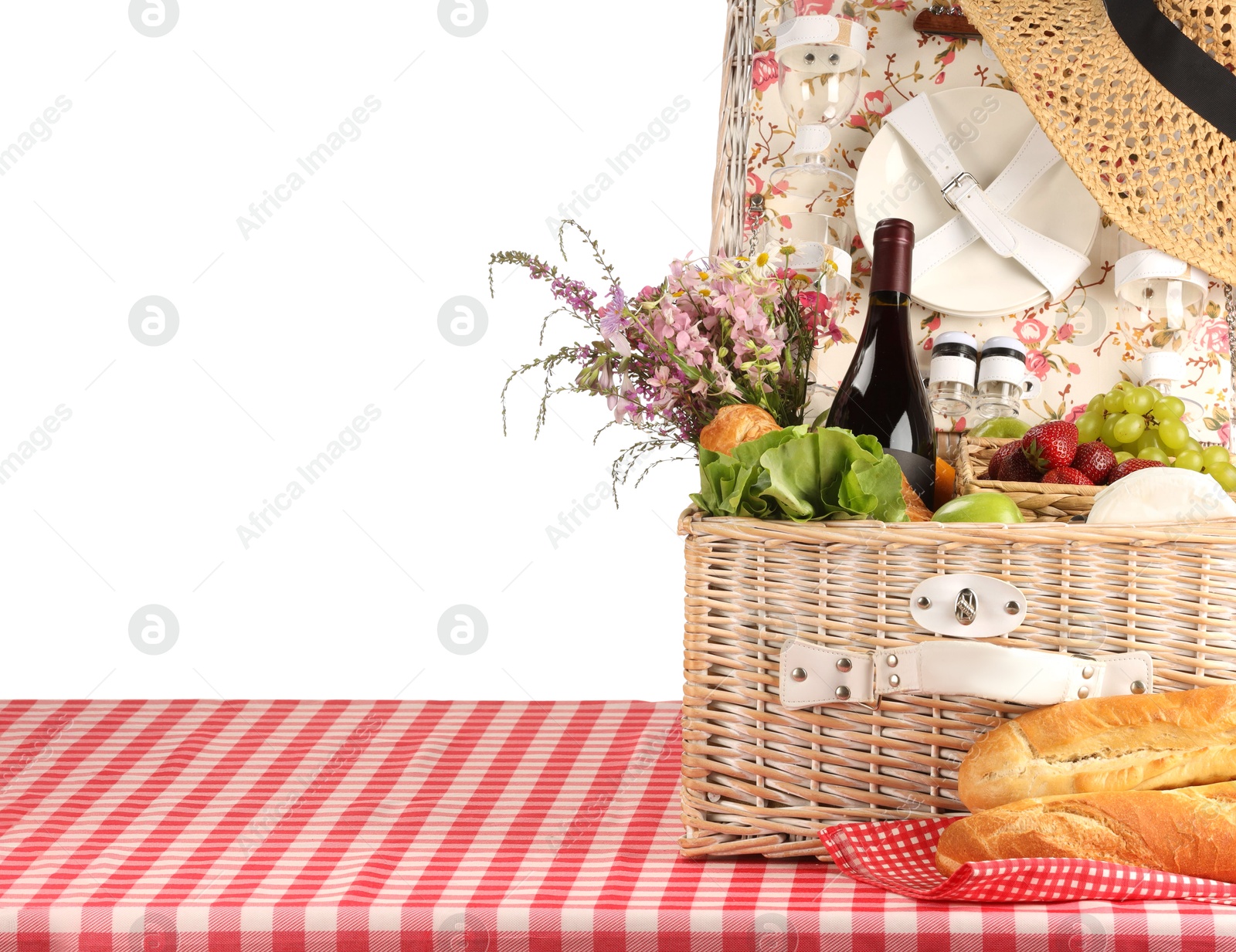 Photo of Picnic wicker basket with food, tableware, bottle of wine and flowers on table against white background. Space for text