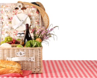 Photo of Picnic wicker basket with food, tableware, bottle of wine and flowers on table against white background. Space for text