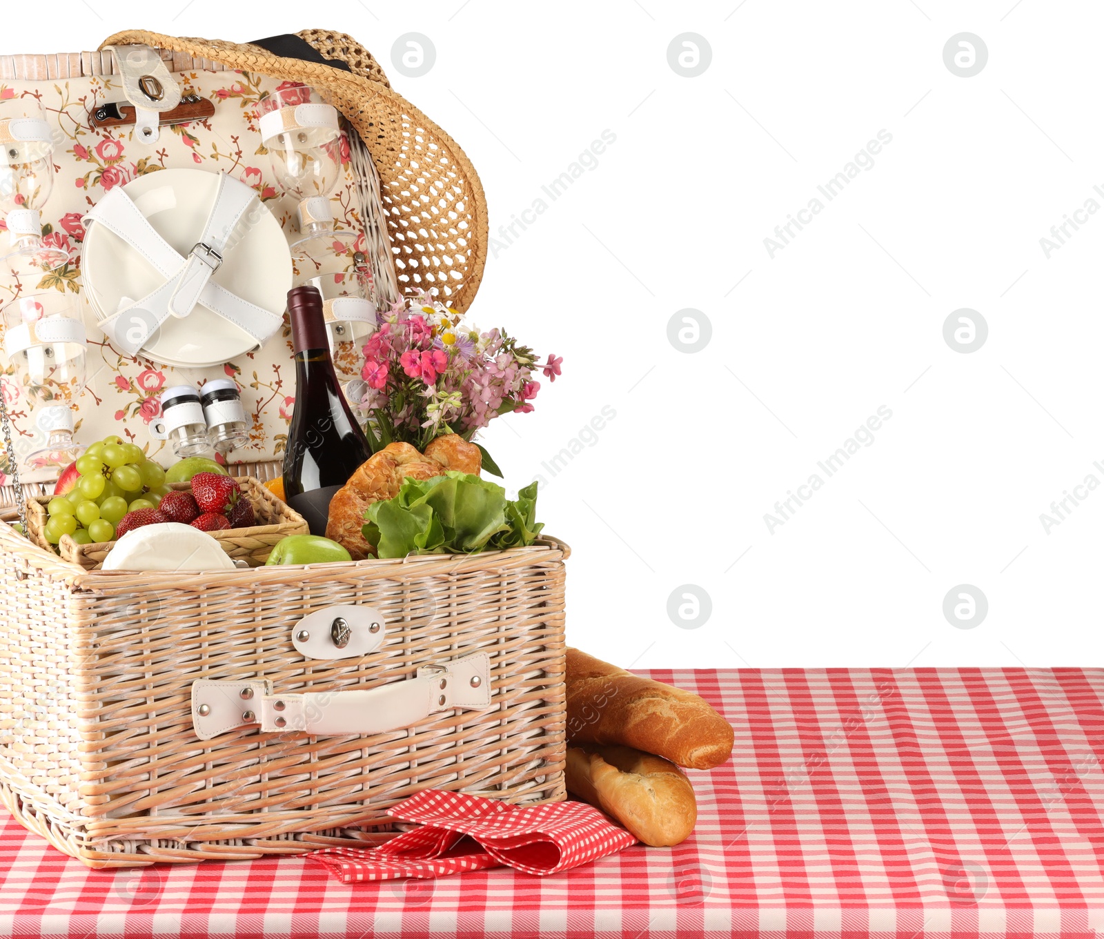 Photo of Picnic wicker basket with food, tableware, bottle of wine and flowers on table against white background. Space for text