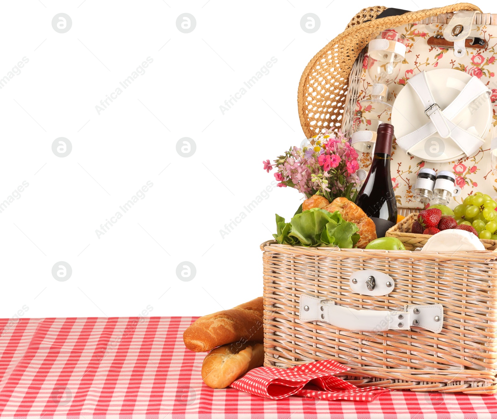 Photo of Picnic wicker basket with food, tableware, bottle of wine and flowers on table against white background. Space for text