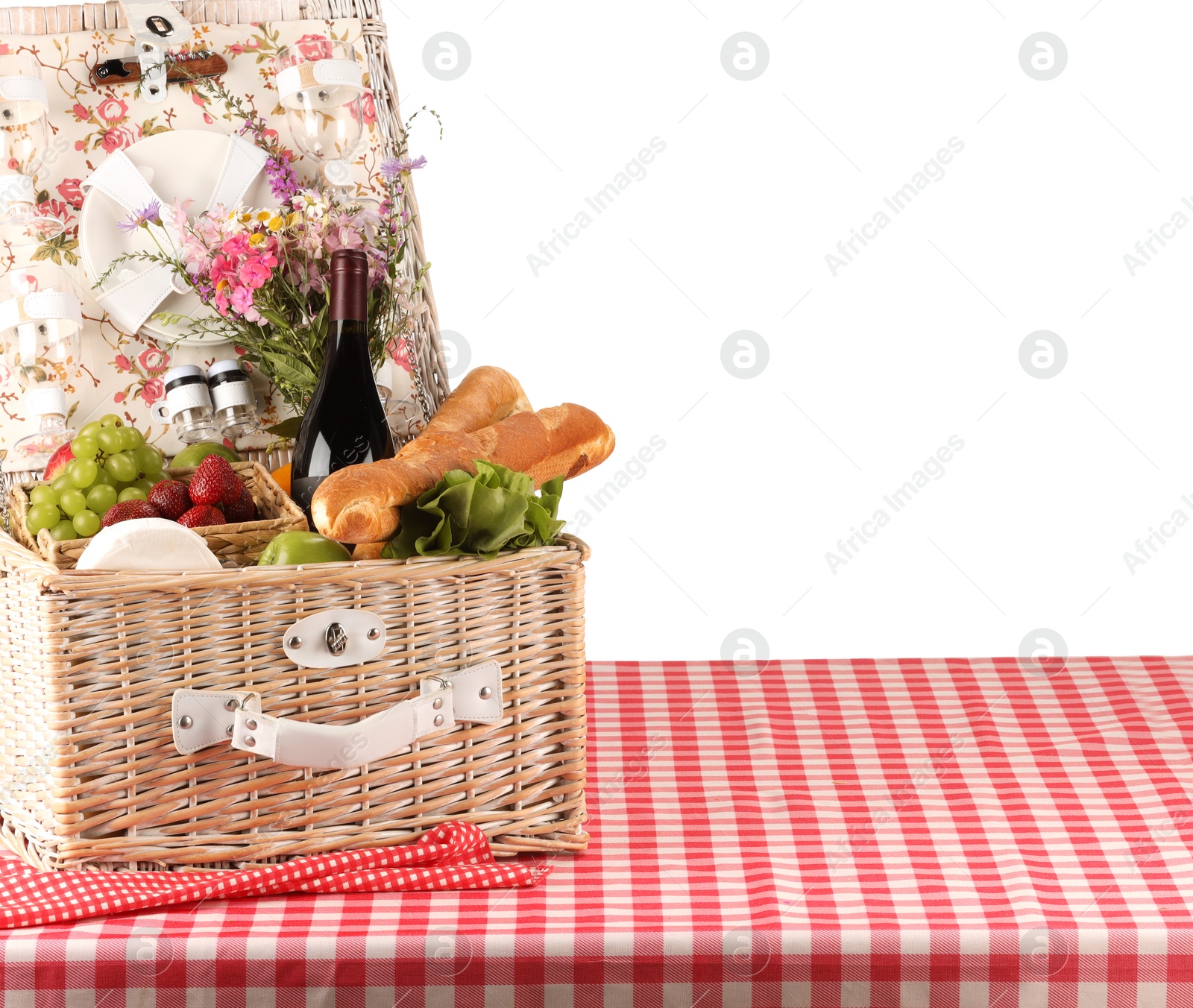 Photo of Picnic wicker basket with food, tableware, bottle of wine and flowers on table against white background. Space for text