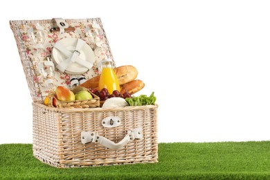 Photo of Picnic wicker basket with food, tableware and bottle of juice on grass against white background. Space for text