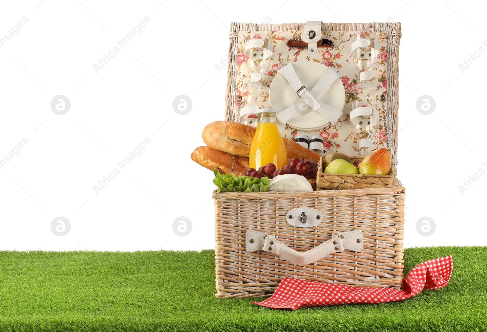 Photo of Picnic wicker basket with food, tableware and bottle of juice on grass against white background. Space for text