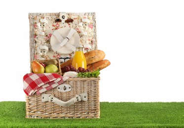 Photo of Picnic wicker basket with food, tableware and bottle of juice on grass against white background. Space for text