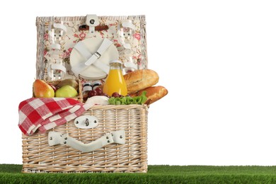 Photo of Picnic wicker basket with food, tableware and bottle of juice on grass against white background. Space for text