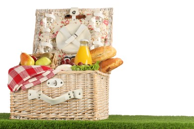 Photo of Picnic wicker basket with food, tableware and bottle of juice on grass against white background. Space for text