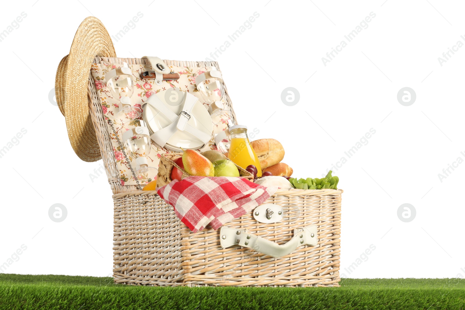 Photo of Picnic wicker basket with food, tableware, bottle of juice and hat on grass against white background. Space for text