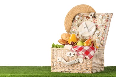 Photo of Picnic wicker basket with food, tableware, bottle of juice and hat on grass against white background. Space for text