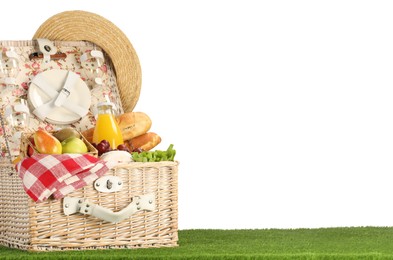 Photo of Picnic wicker basket with food, tableware, bottle of juice and hat on grass against white background. Space for text