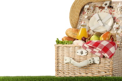 Photo of Picnic wicker basket with food, tableware, bottle of juice and hat on grass against white background. Space for text