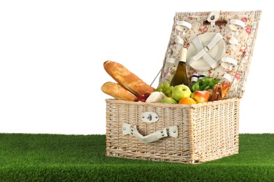 Picnic wicker basket with food, tableware and bottle of wine on grass against white background. Space for text