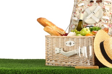 Photo of Picnic wicker basket with food, tableware, bottle of wine and hat on grass against white background. Space for text