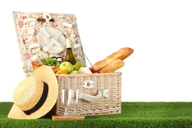 Picnic wicker basket with food, tableware, bottle of wine and hat on grass against white background. Space for text