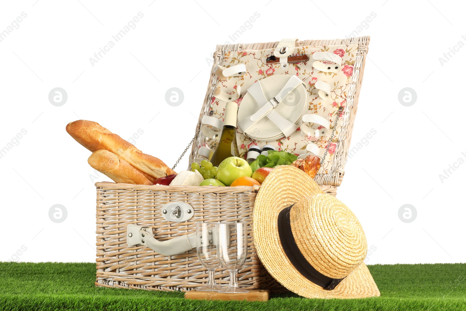 Photo of Picnic wicker basket with food, tableware, bottle of wine and hat on grass against white background