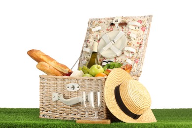 Photo of Picnic wicker basket with food, tableware, bottle of wine and hat on grass against white background