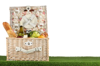 Photo of Picnic wicker basket with food, tableware, bottle of wine and hat on grass against white background. Space for text