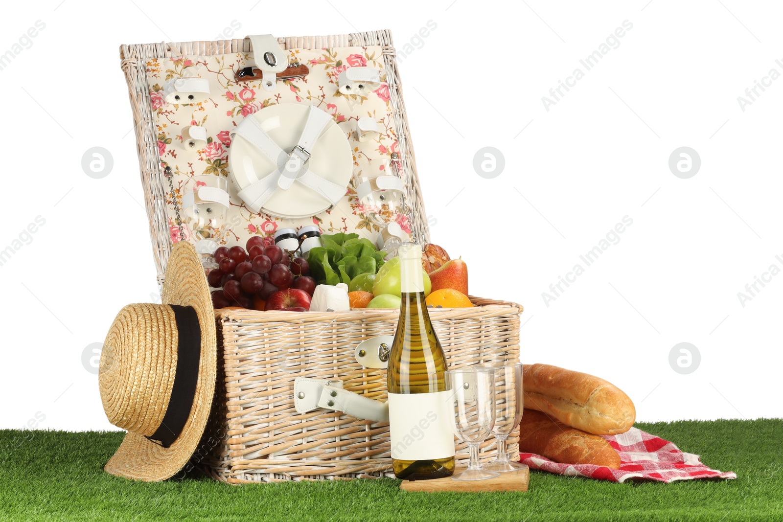 Photo of Picnic wicker basket with food, tableware, bottle of wine and hat on grass against white background