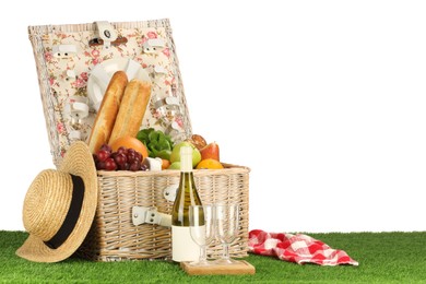 Photo of Picnic wicker basket with food, tableware, bottle of wine and hat on grass against white background. Space for text