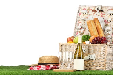 Photo of Picnic wicker basket with food, tableware, bottle of wine and hat on grass against white background. Space for text