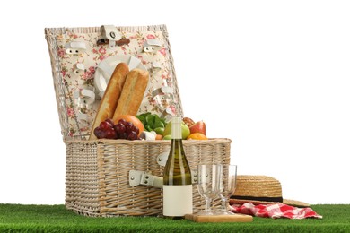 Photo of Picnic wicker basket with food, tableware, bottle of wine and hat on grass against white background