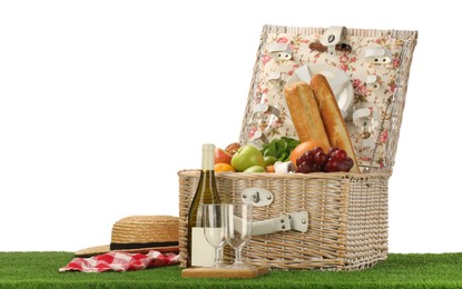 Photo of Picnic wicker basket with food, tableware, bottle of wine and hat on grass against white background. Space for text