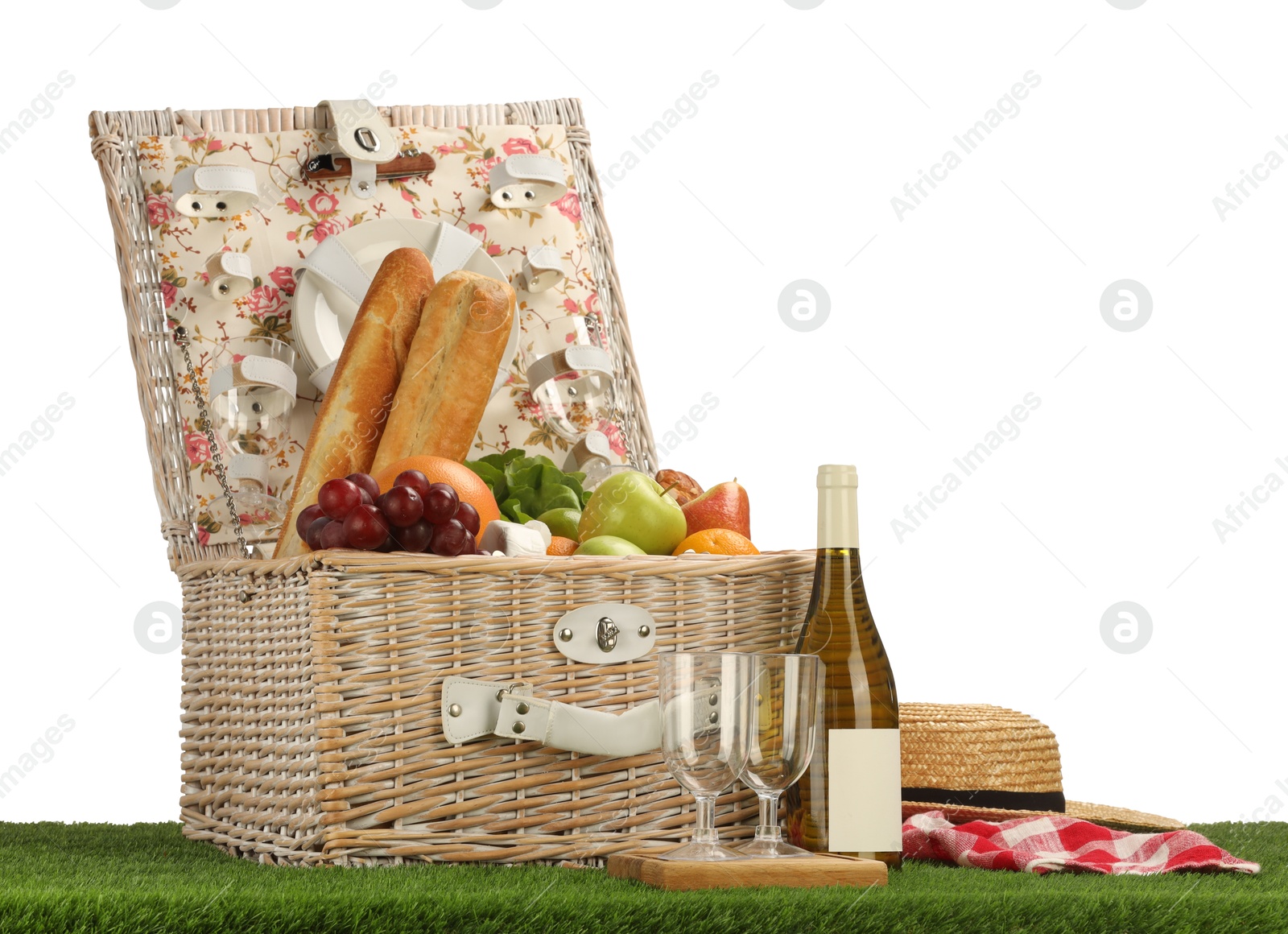 Photo of Picnic wicker basket with food, tableware, bottle of wine and hat on grass against white background