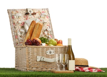 Photo of Picnic wicker basket with food, tableware, bottle of wine and hat on grass against white background