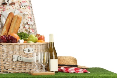 Picnic wicker basket with food, tableware, bottle of wine and hat on grass against white background. Space for text