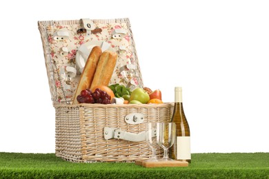 Photo of Picnic wicker basket with food, tableware, bottle of wine and glasses on grass against white background