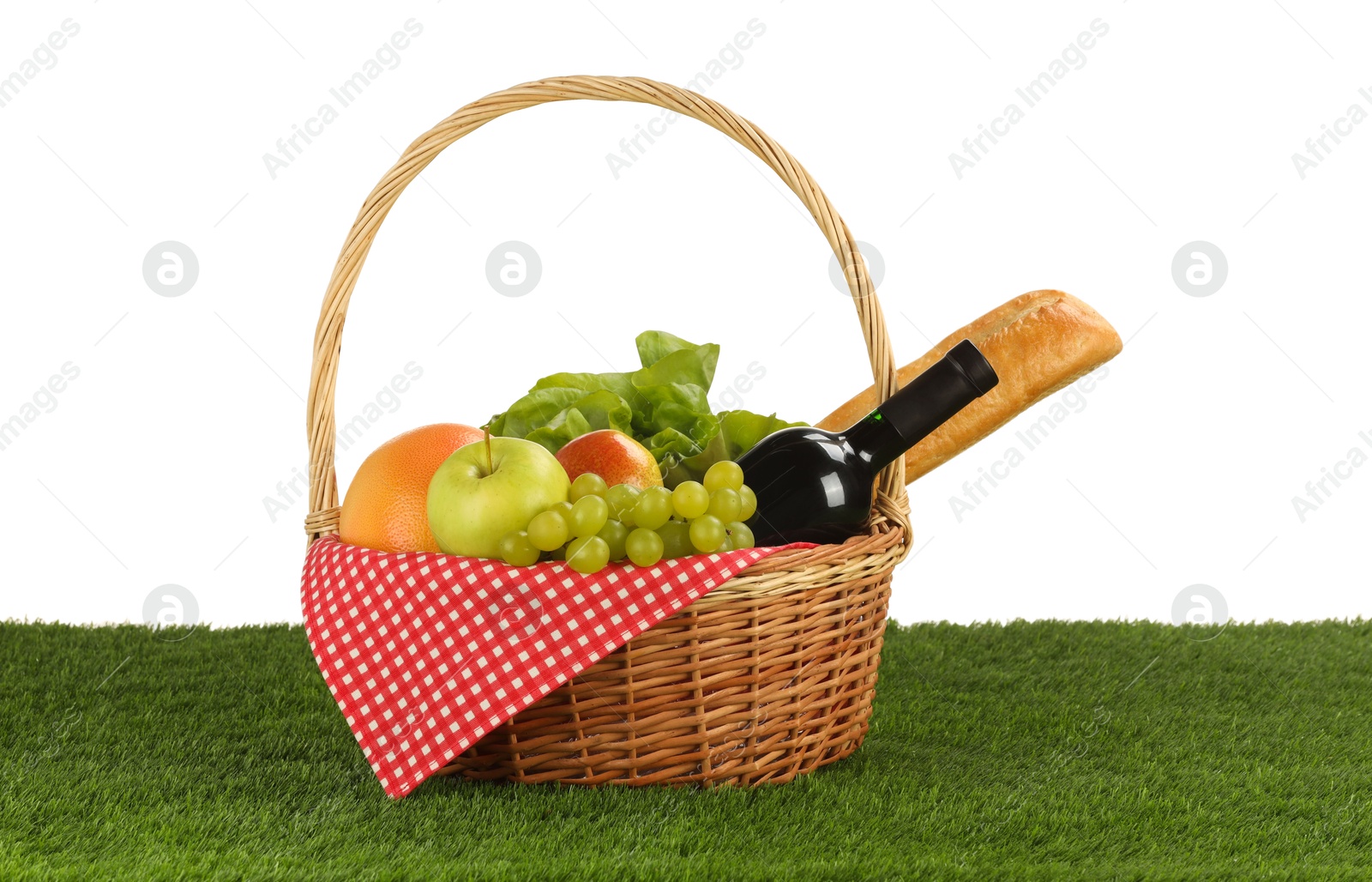 Photo of Picnic wicker basket with food and bottle of wine on grass against white background