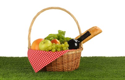 Photo of Picnic wicker basket with food and bottle of wine on grass against white background